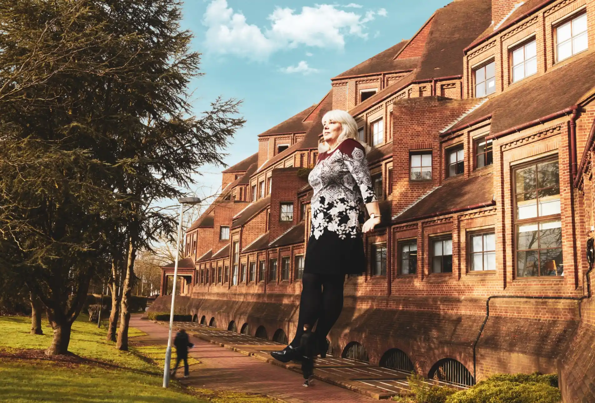 Giant woman leans against a sun-soaked residential building.