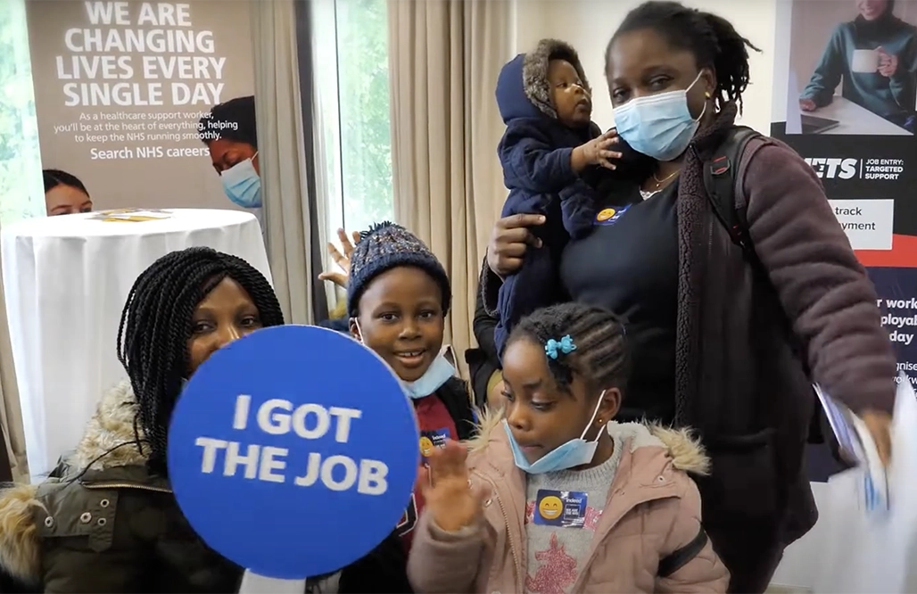 NHS England - A woman with her 4 kids holding a sign 